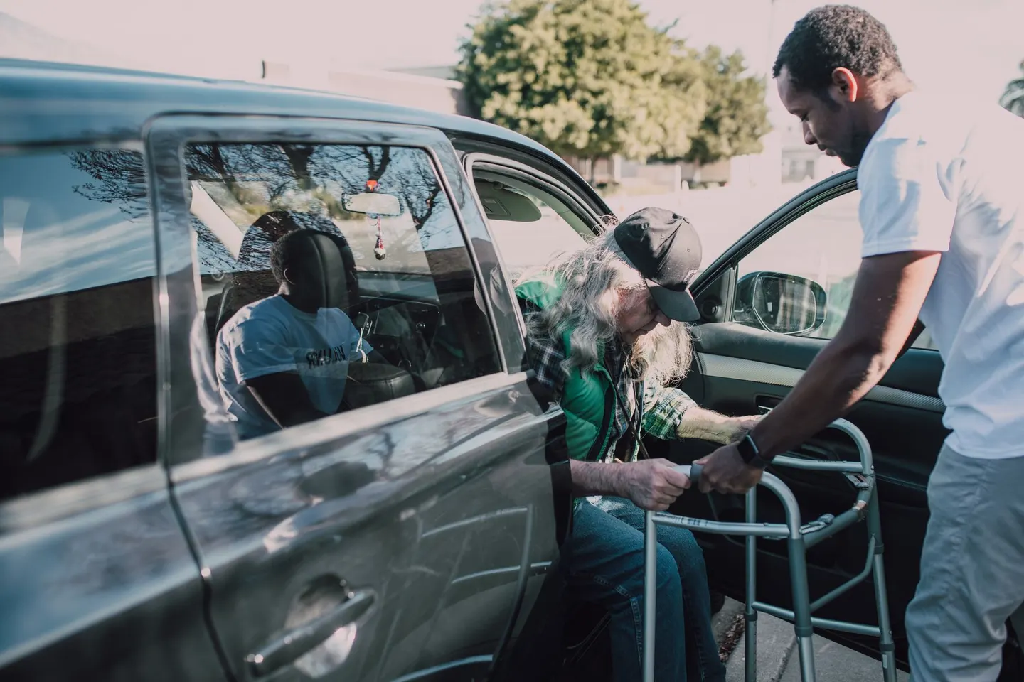 Caregiver helping an older adult with a walker out of a car