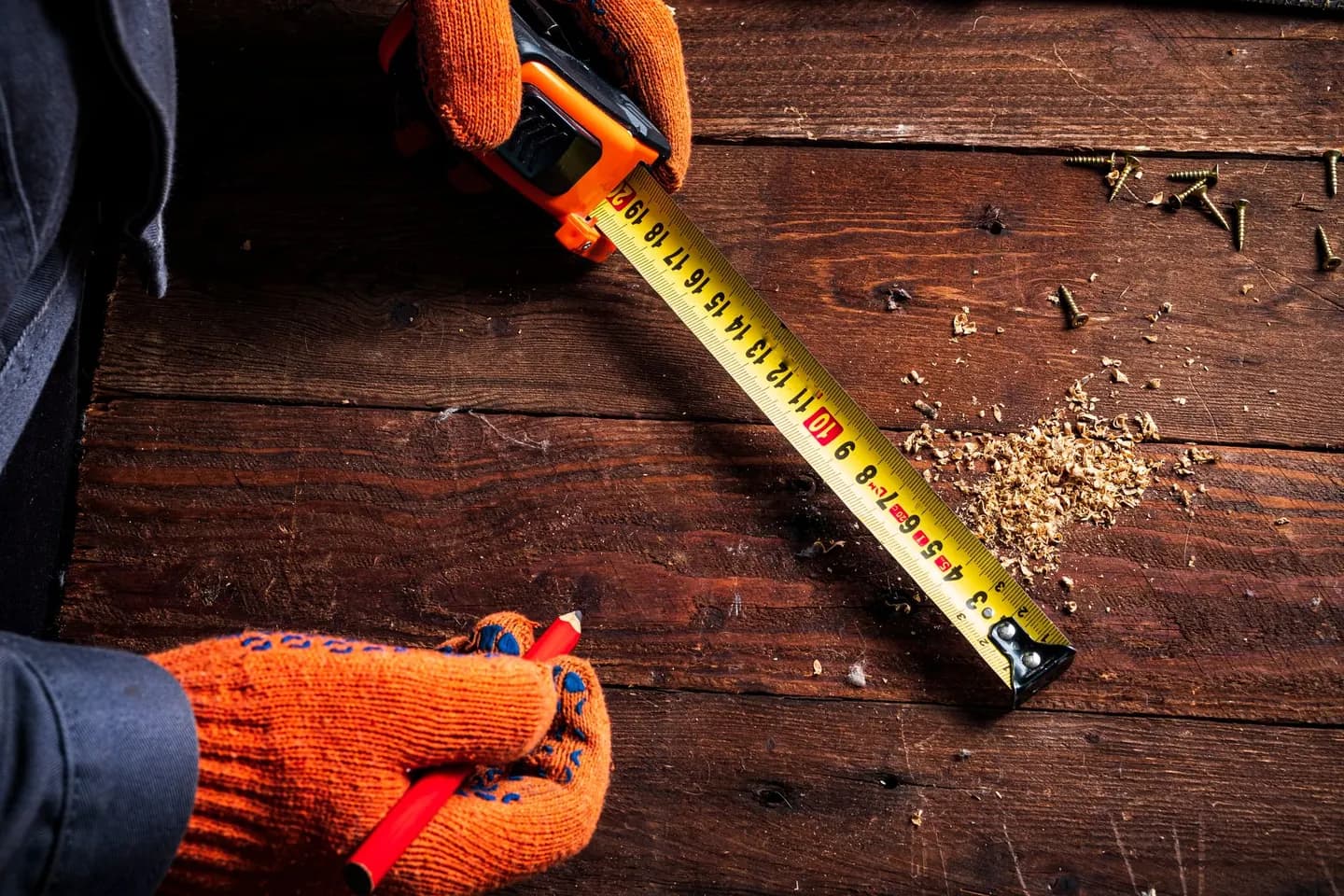 Close-up of gloved hands using a tape measure on wooden surface for precise carpentry