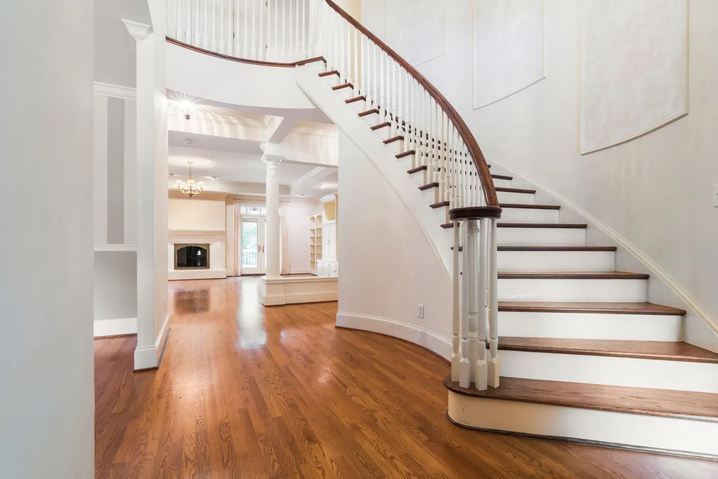 Bright and spacious luxury home interior featuring a grand curved staircase and hardwood floors