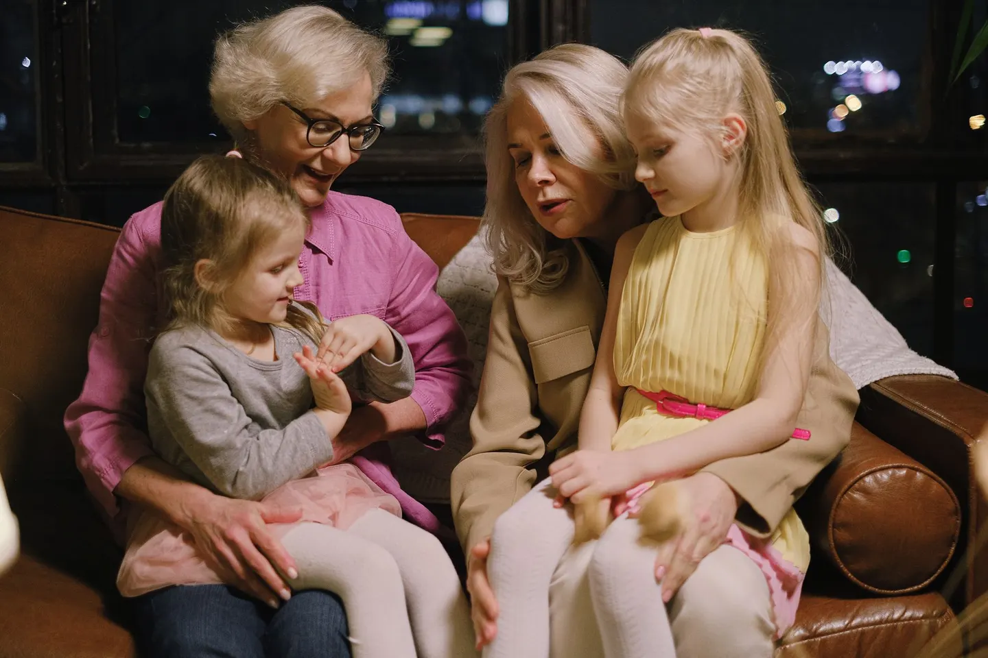 A warm family moment indoors with two grandmothers and two granddaughters sitting together on a sofa