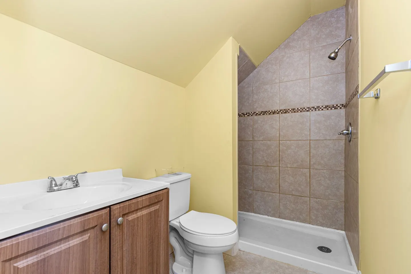 A small bathroom with a tiled walk-in shower, a toilet and a wood vanity