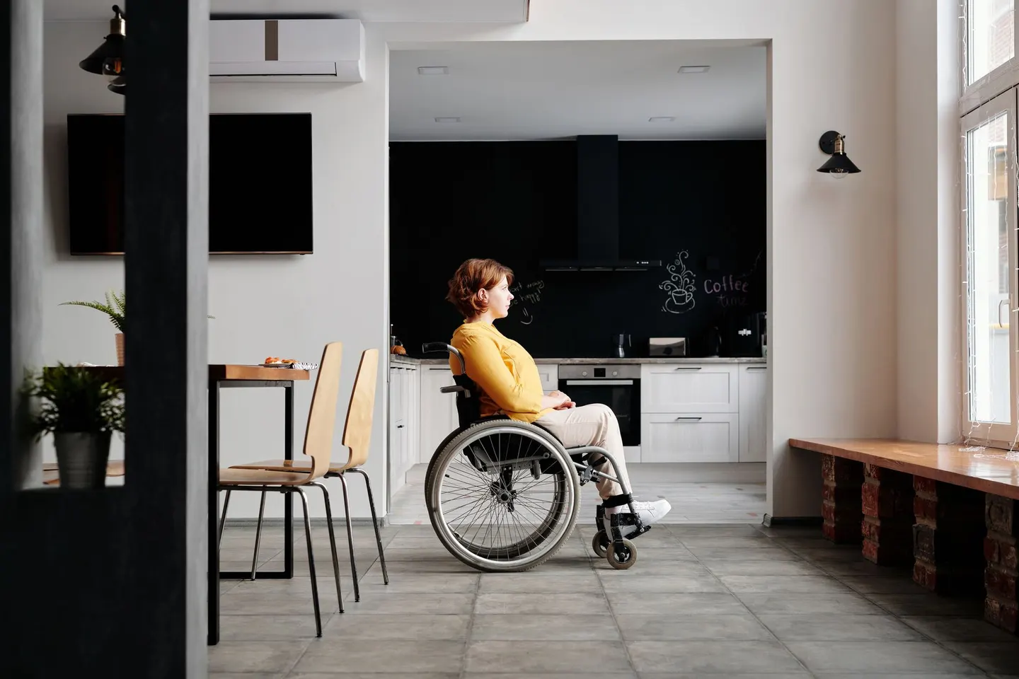 Woman using a wheelchair beside a wide doorway into a kitchen